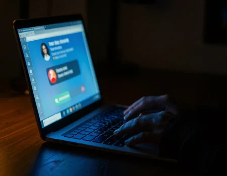 Person receiving an AI voice scam call on a laptop in a dark room — cybersecurity threats 2026