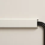 A person using a paintable cord cover to neatly hide a TV power cord against a white wall.